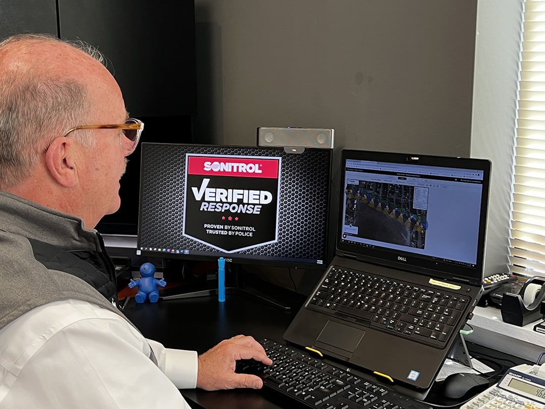 A System Surveyor employee at a computer workstation with two screens watching a video on one screen and a Sonitrol logo graphic appears on the other computer screen.